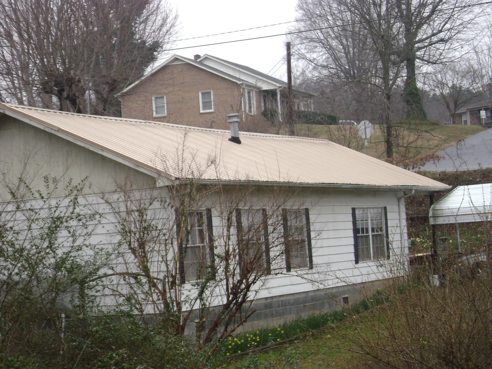 Tan metal roof on a white sided house set into a hillside — Commercial Roofing by Roofing Brothers in Valley